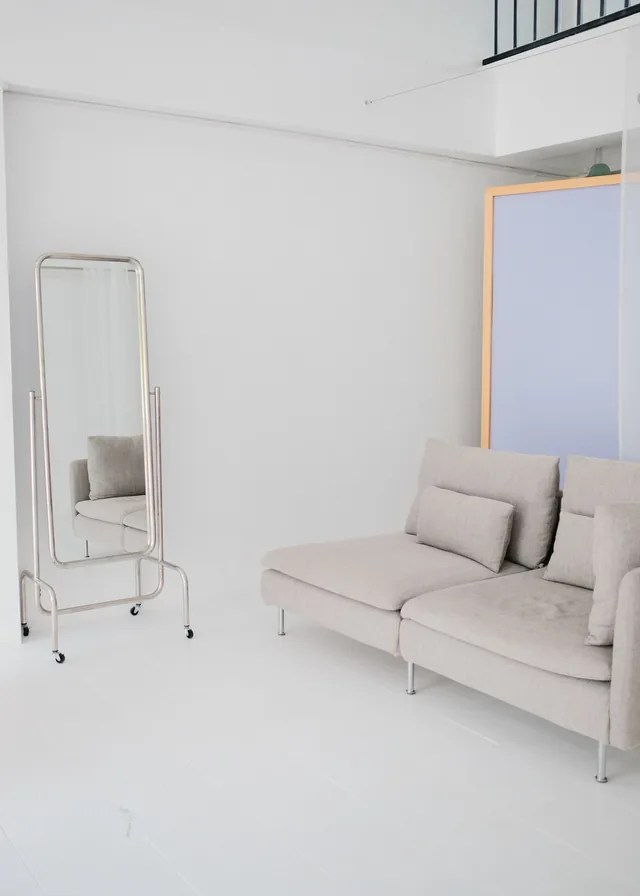 Floor mirror beside a grey sofa and lilac backdrop